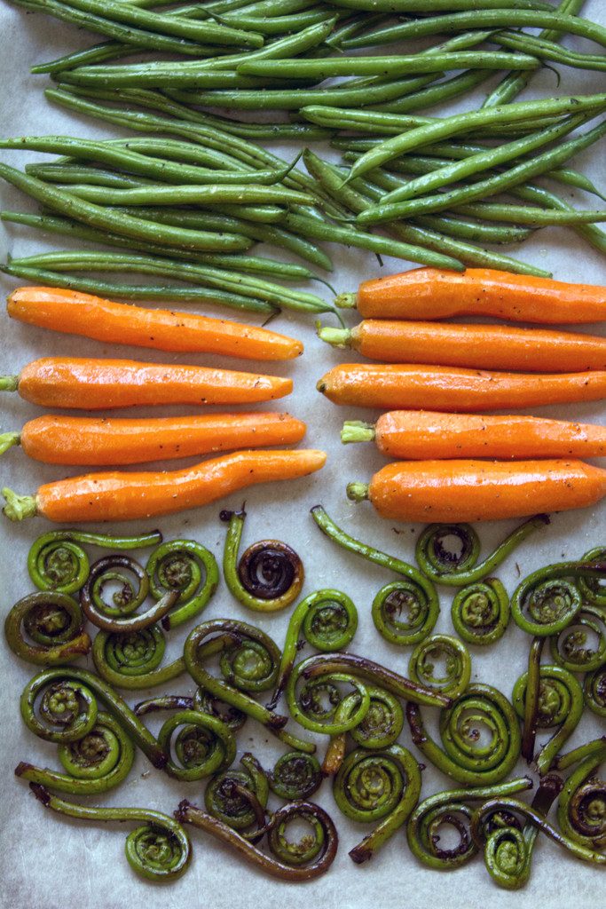 Overhead view of baking pan with fiddleheads, heirloom carrots, and haricot vert ready to be roasted