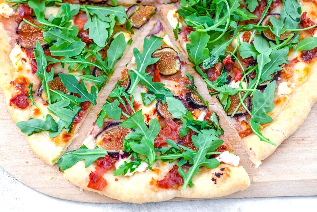 Landscape overhead closeup view of a slice of fig, prosciutto, and goat cheese flatbread topped with arugula 