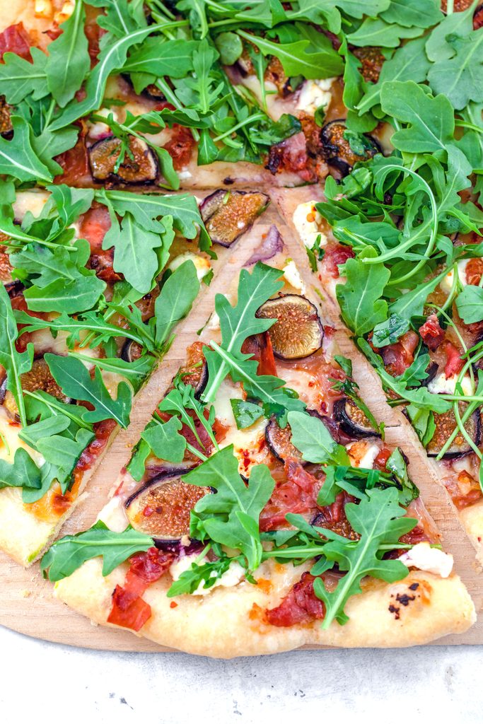 Overhead view of a slice of fig, prosciutto, and goat cheese flatbread topped with arugula and pulled out from the rest of the pizza