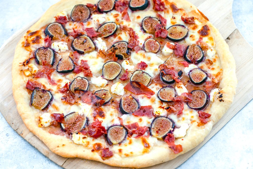 Landscape overhead view of fig, prosciutto, and goat cheese flatbread right out of the oven on pizza peel