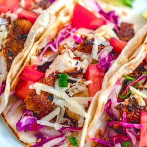 Closeup view of a fish taco topped with cheese, tomatoes, and red onion and cabbage slaw