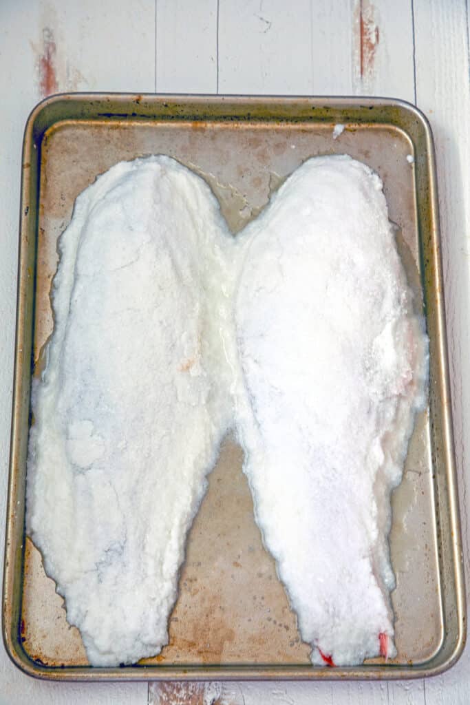 Overhead view of baking pan with two salt-covered whole fish before baking.