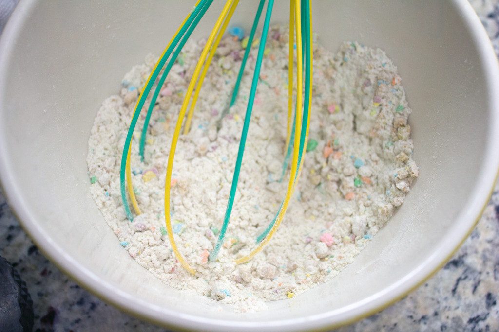 Overhead view of dry ingredients for Lucky Charms doughnuts in a bowl with a whisk