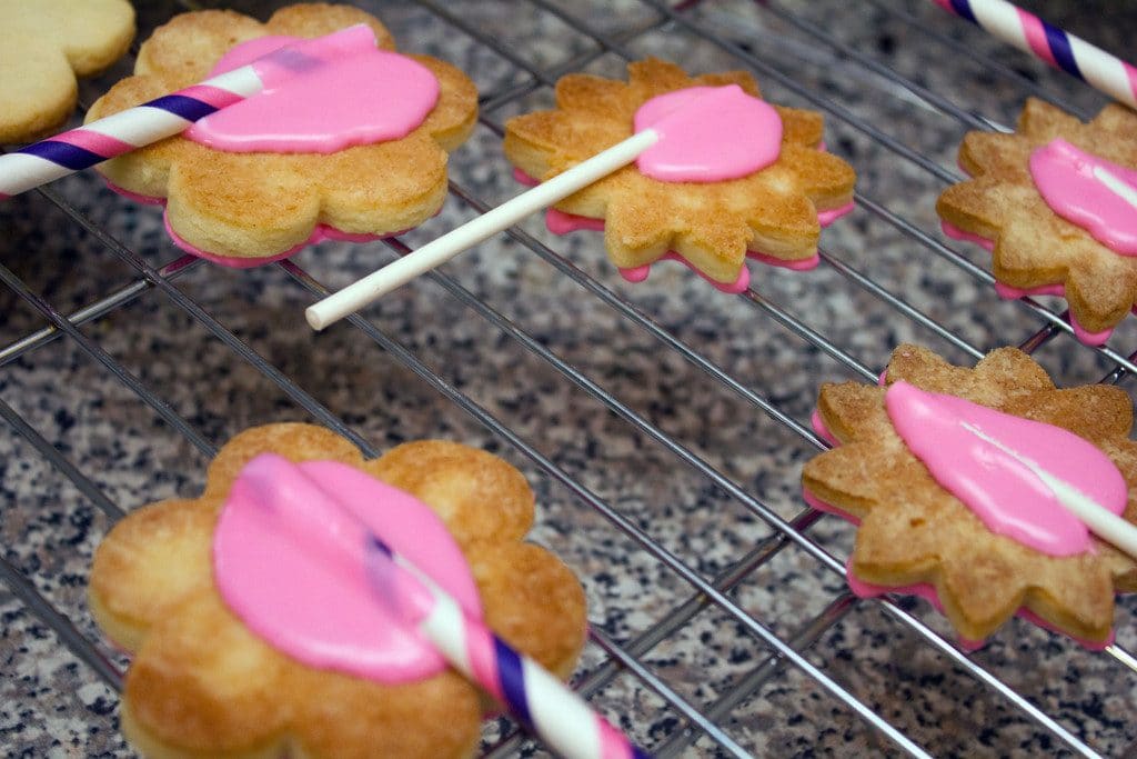 Overhead view of frosted flower sugar cookies upside down with straws glued to the back with royal icing