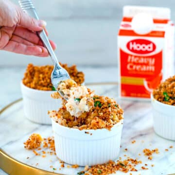 Head-on view of ramekin of mac and cheese with panko breadcrumbs and hand taking a forkful out.