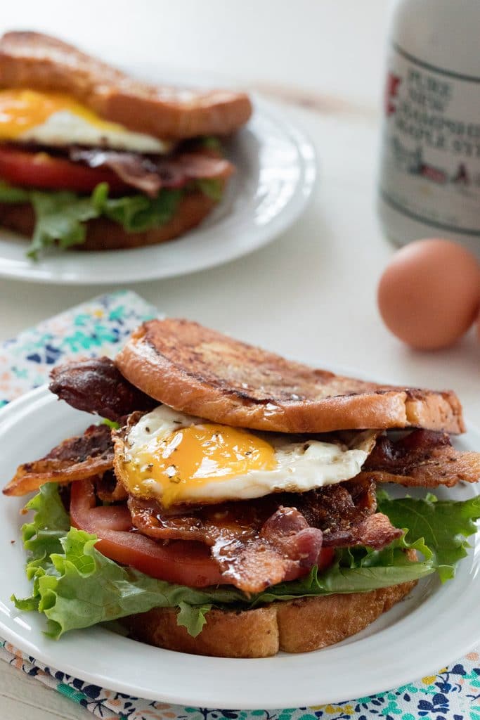 Overhead view of a french toast BLT sandwich with second sandwich, eggs, and maple syrup in background