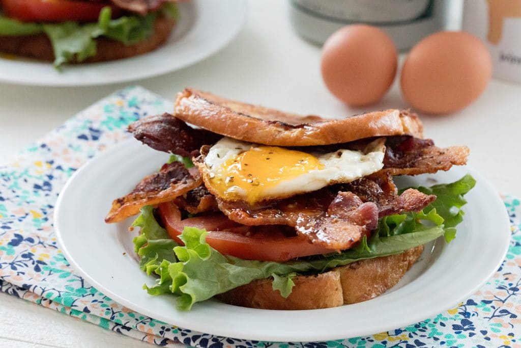 Landscape head-on view of a french toast BLT with eggs and maple syrup in background