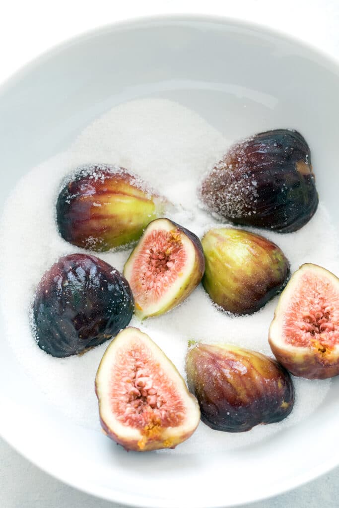 Overhead view of a bowl of granulated sugar with halved fresh figs in it