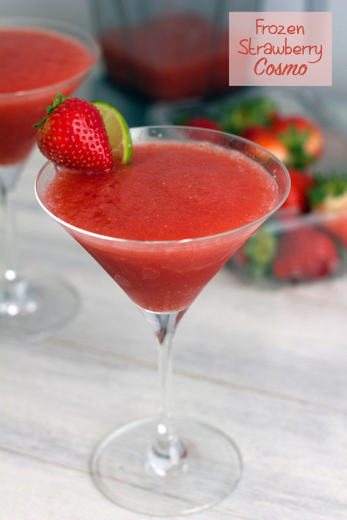 Head-on view of frozen strawberry cosmo with strawberry lime garnish, another cosmo and strawberries in the background, and "Frozen Strawberry Cosmo" text at top