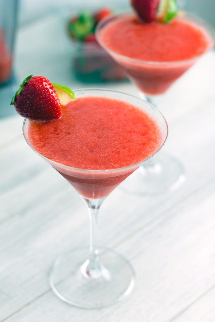 Head-on view of two frozen strawberry cosmos in martini glasses with strawberry and lime garnish