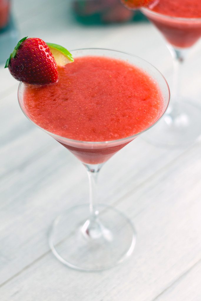 Close-up of a frozen strawberry cosmo in a martini glass with strawberry and lime garnish