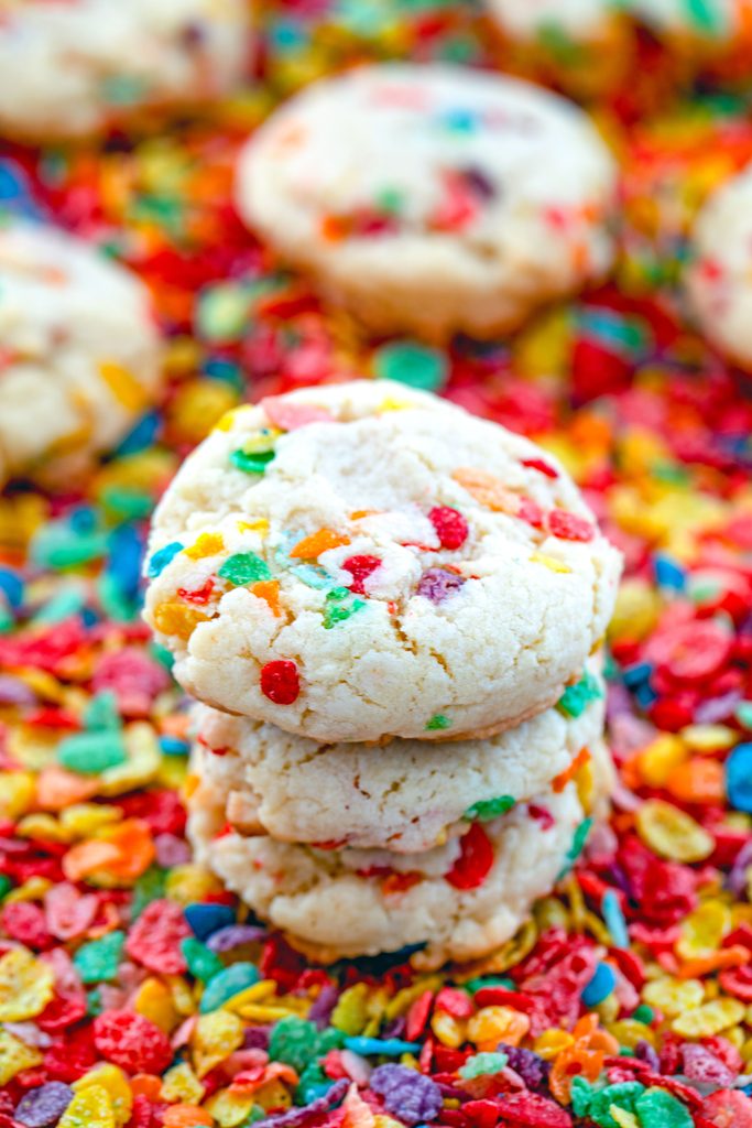 View of three Fruity Pebbles cookies stacked on top of each other on a bed of the cereal with more cookies in the background