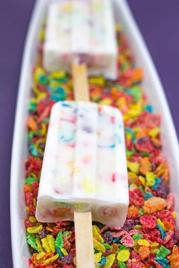 Closeup of Fruity Pebbles Greek yogurt popsicles facing up on a bed of Fruity Pebbles