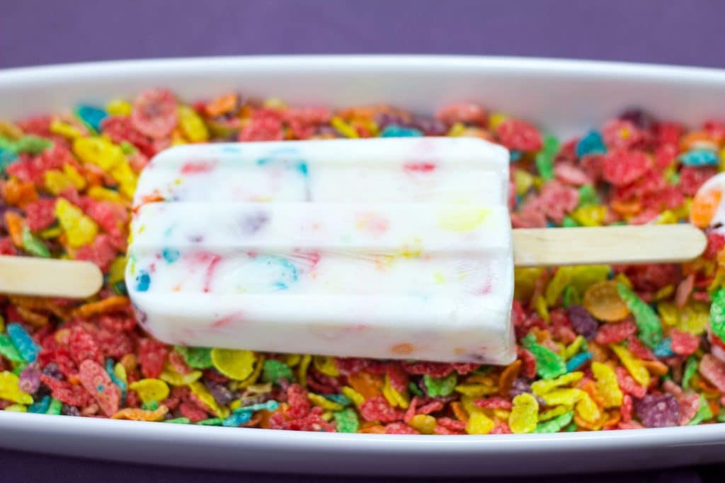 Horizontal image of a closeup of Fruity Pebbles Greek yogurt popsicle on a bed of Fruity Pebbles