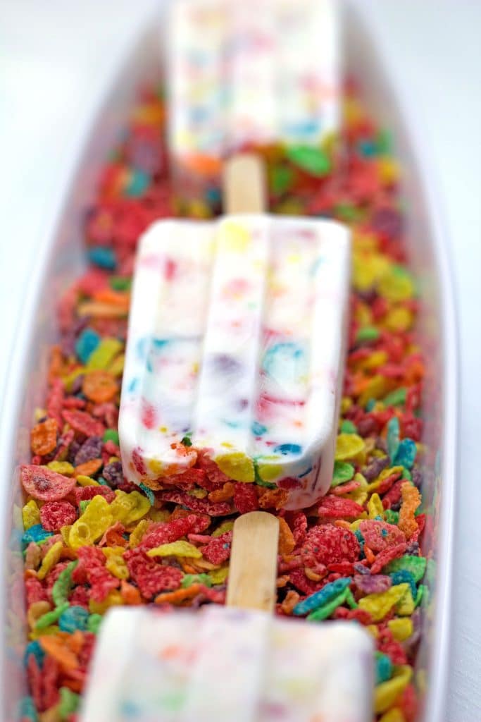 Row of Fruity Pebbles Greek yogurt popsicles facing down on a bed of Fruity Pebbles