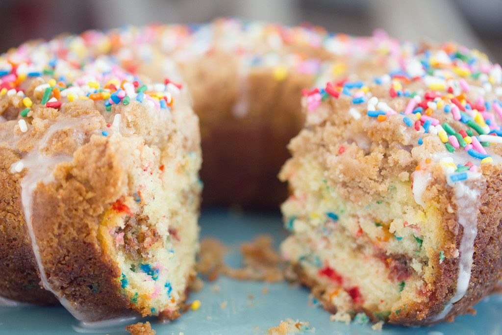 Closeup view of funfetti coffee cake sitting on a cake plate with a large slice removed