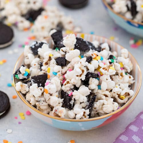 Head-on closeup view of Oreo funfetti popcorn with colorful sprinkles in a bowl with Oreo cookies and more popcorn and sprinkles in background