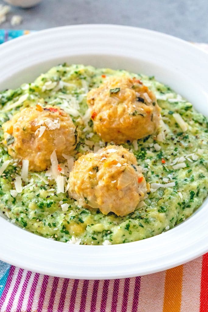 Head on view of white bowl filled with kale polenta and topped with three chicken meatballs on a colorful placemat