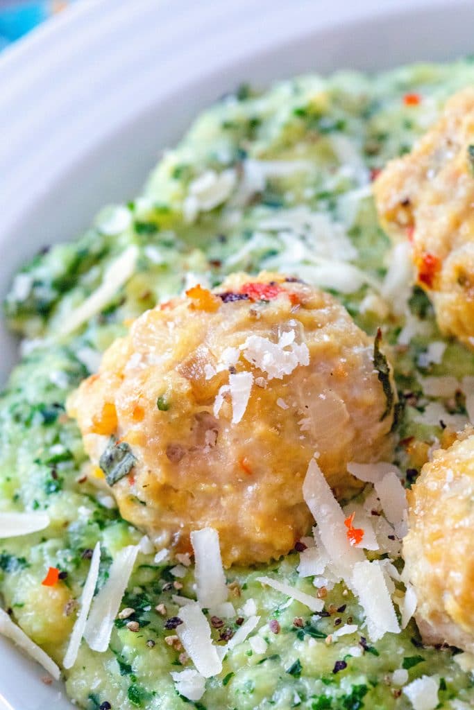 Closeup of a garlic habanero chicken meatball on top of kale polenta with grated parmesan cheese