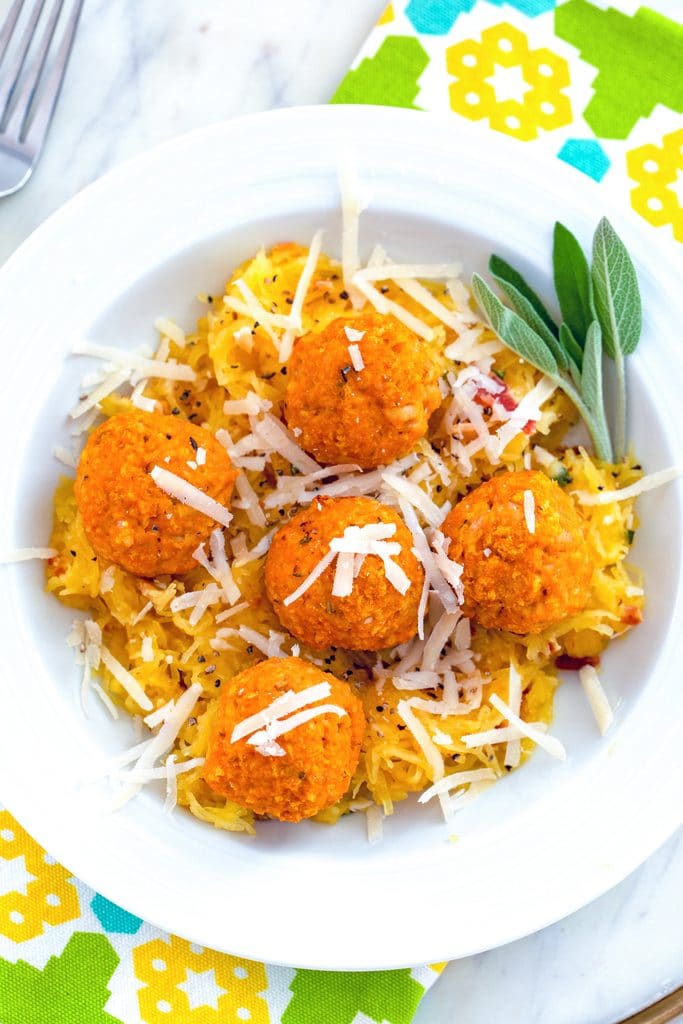 Overhead view of garlicky spaghetti squash in a white bowl with chicken pumpkin meatballs and parmesan cheese on top with sage