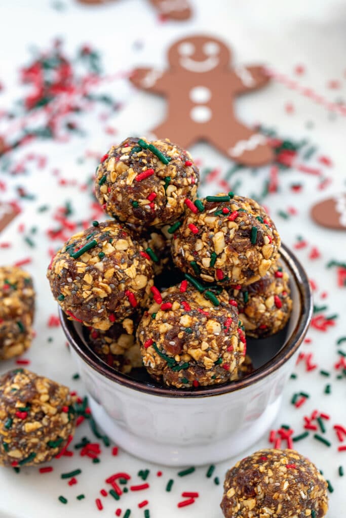 Head-on view of a small bowl of gingerbread energy balls with energy bites and red and green sprinkles all around and gingerbread man at top