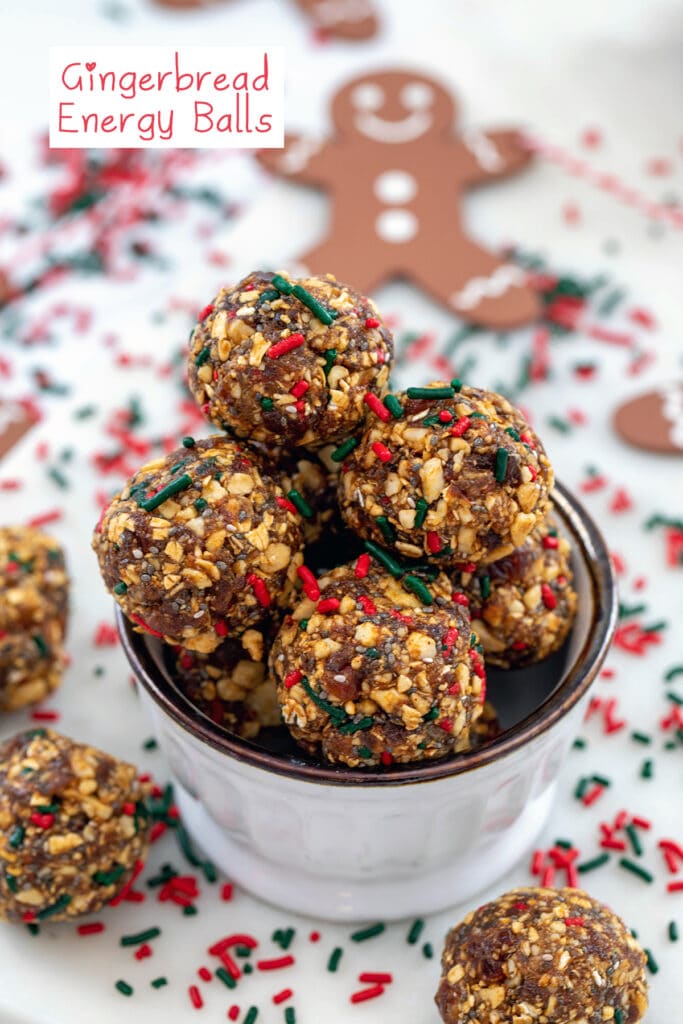 Head-on view of a small bowl of gingerbread energy balls with energy bites and red and green sprinkles all around and gingerbread man and recipe title at top