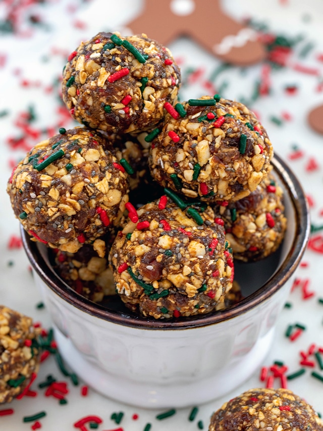 Head-on closeup view of a small bowl of gingerbread energy balls with energy bites and red and green sprinkles all around and gingerbread man at top