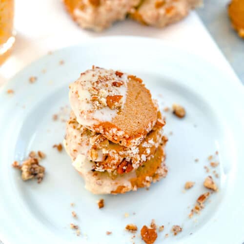 Overhead closeup view of a stack of three gingerbread shortbread cookies with eggnog glaze and pecans on a white plate with pecan crumbles