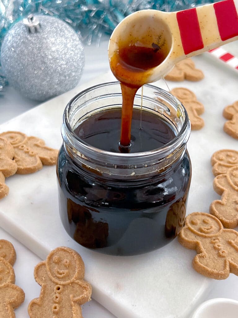 Gingerbread syrup drizzling off spoon into jar with small gingerbread men all around.