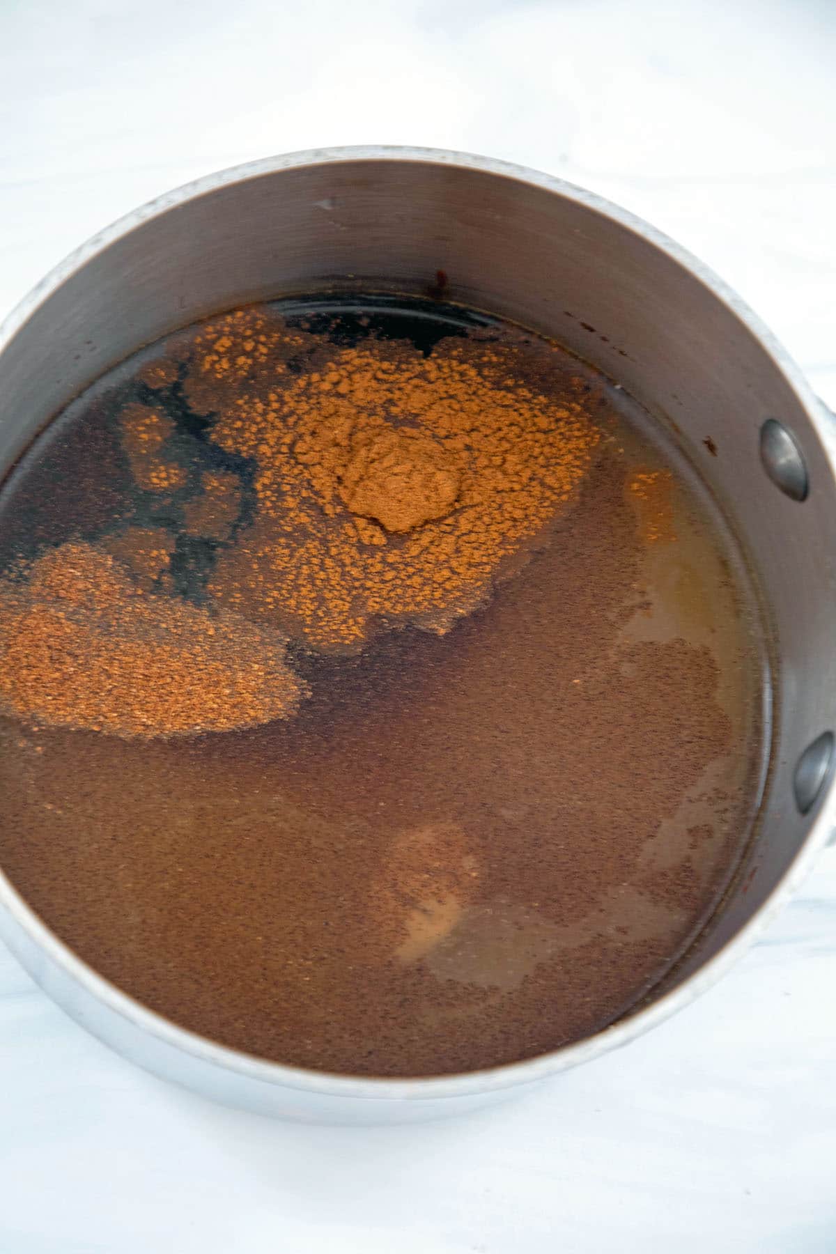 Overhead view of water and sugar in saucepan with gingerbread spices being mixed in.