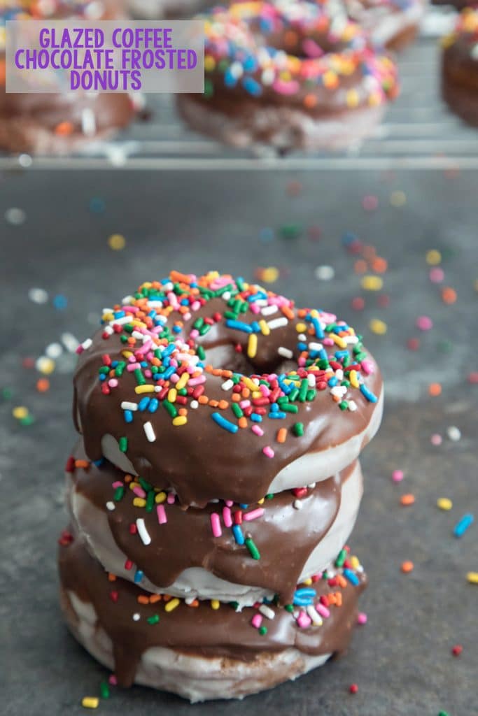 Head-on view of a stack of three glazed coffee chocolate frosted donuts with sprinkles with a baking rack with more donuts in the background and recipe title at top