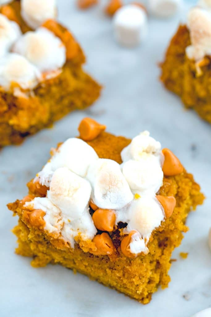 Overhead view of multiple pumpkin butterscotch blondies topped with marshmallows on a white surface