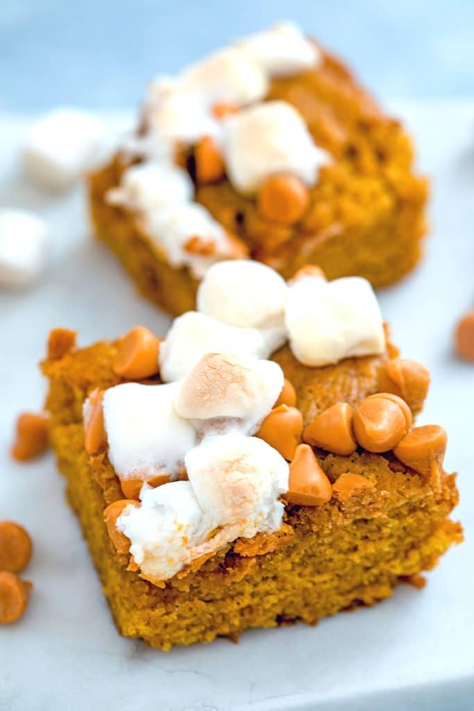 Close-up of two pumpkin butterscotch blondies topped with mini marshmallows on a white surface