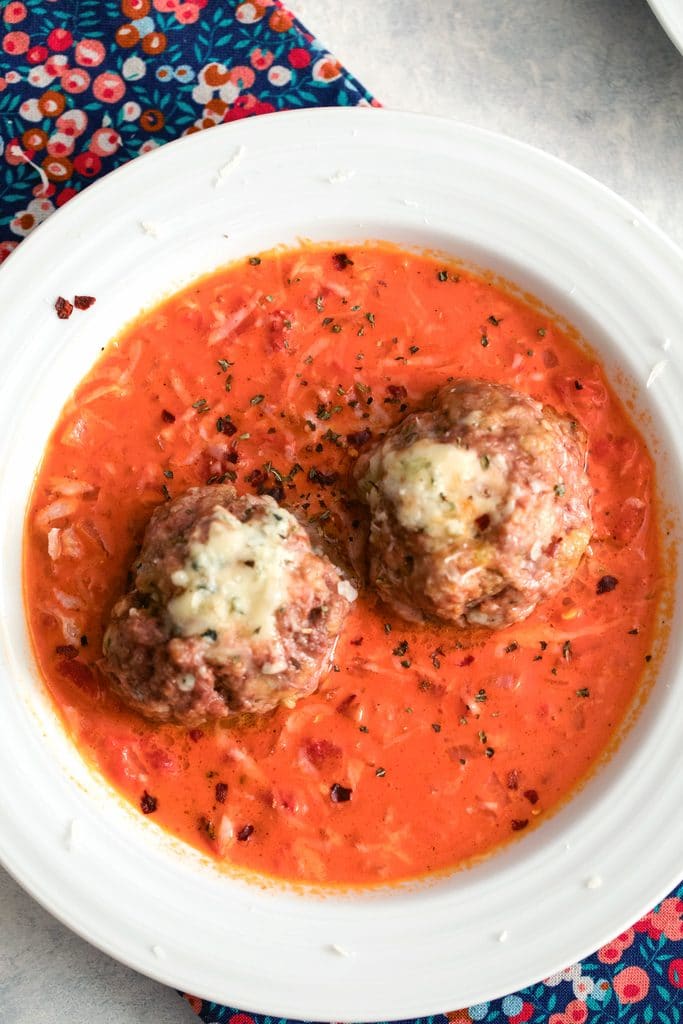 Overhead view of two gorgonzola meatballs over a creamy tomato gravy in a white bowl