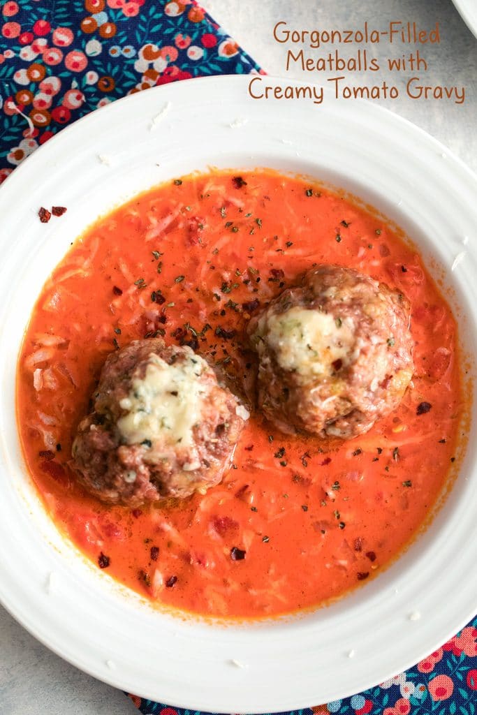 Overhead view of two gorgonzola meatballs over a creamy tomato gravy in a white bowl with recipe title at top