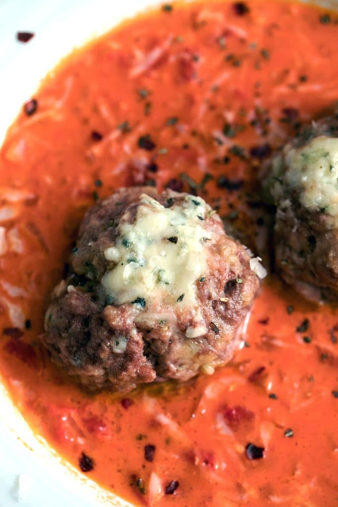 Overhead close-up view of a gorgonzola meatball in a creamy tomato sauce in a white bowl