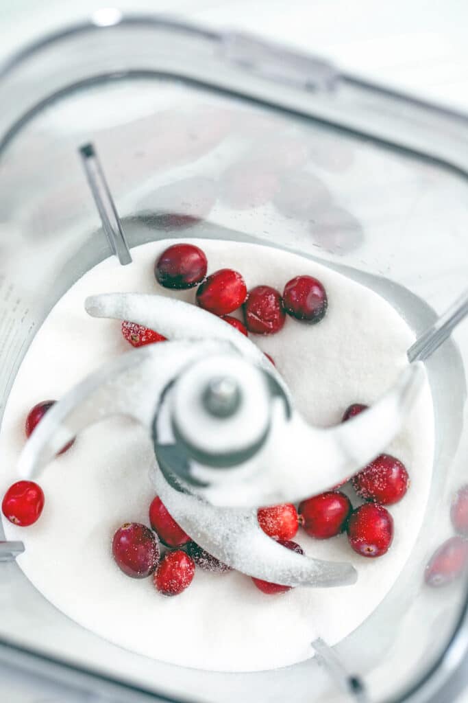 Overhead view of granulated sugar and fresh cranberries in blender