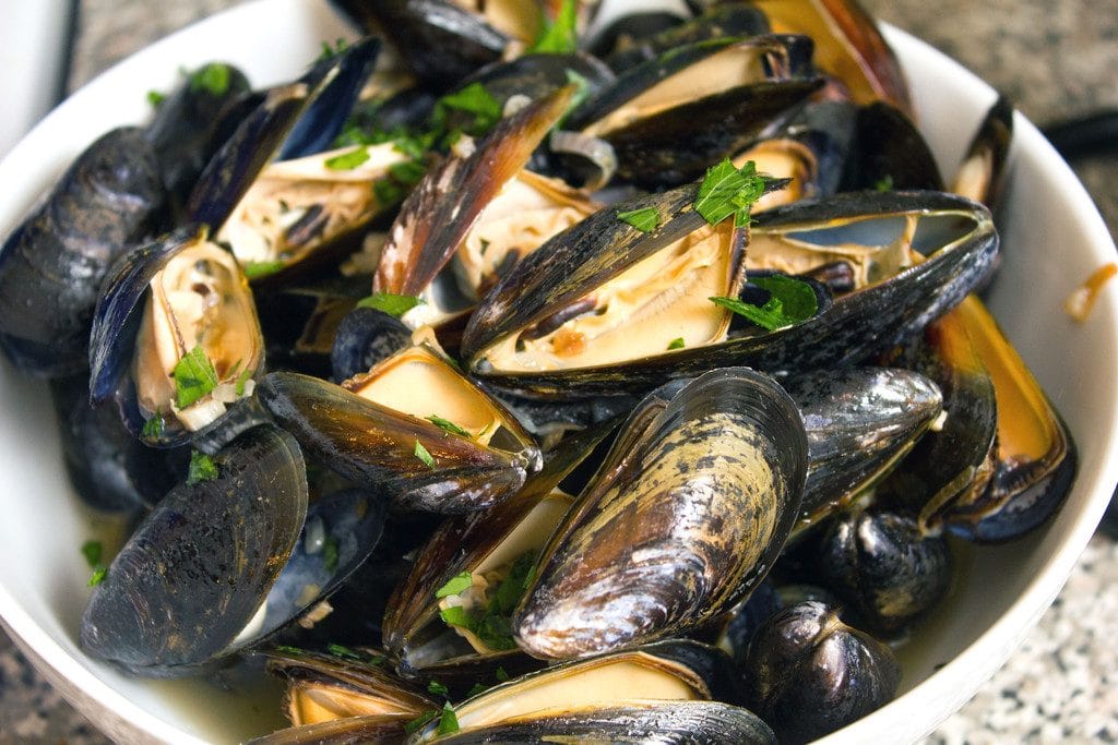 Landscape view of mussels in a white bowl, cooked  and topped with parsley