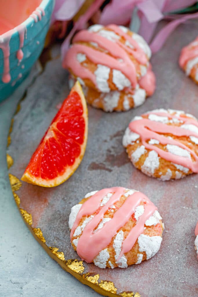 Multiple grapefruit crinkle cookies on platter with grapefruit wedge and bowl of Campari icing in background