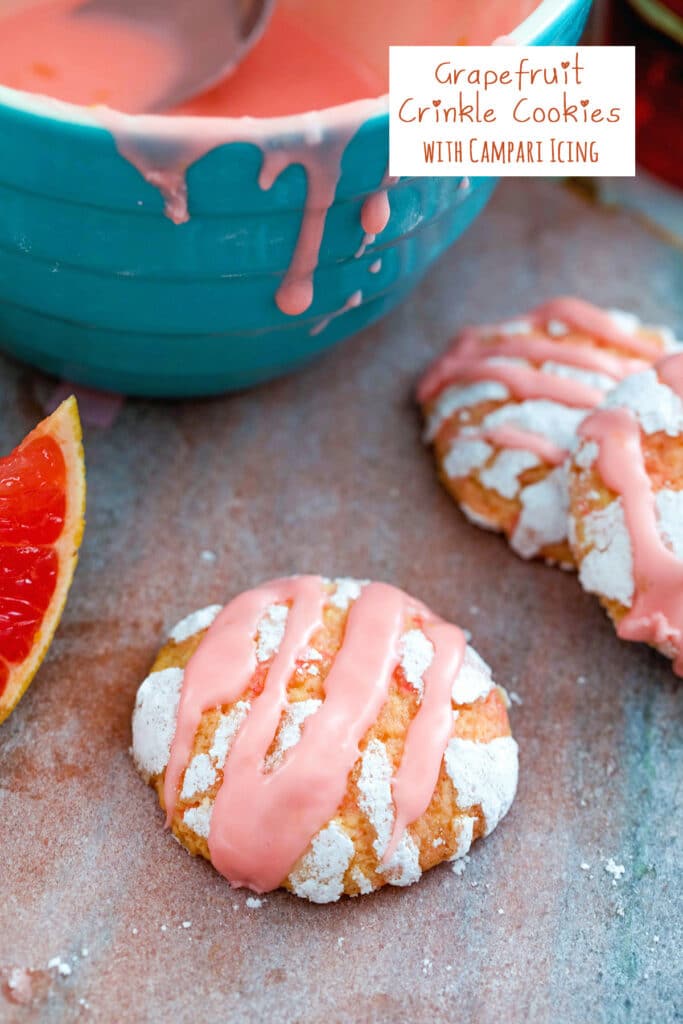 Overhead view of a grapefruit crinkle cookie with grapefruit wedge, bowl of Campari icing, and more cookies in background and recipe title at top
