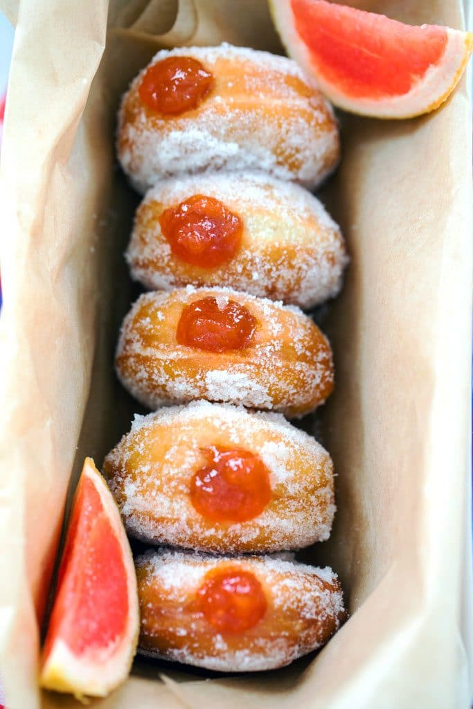 Bird's-eye view of five sugared donuts filled with grapefruit jam in a row in a loaf pan