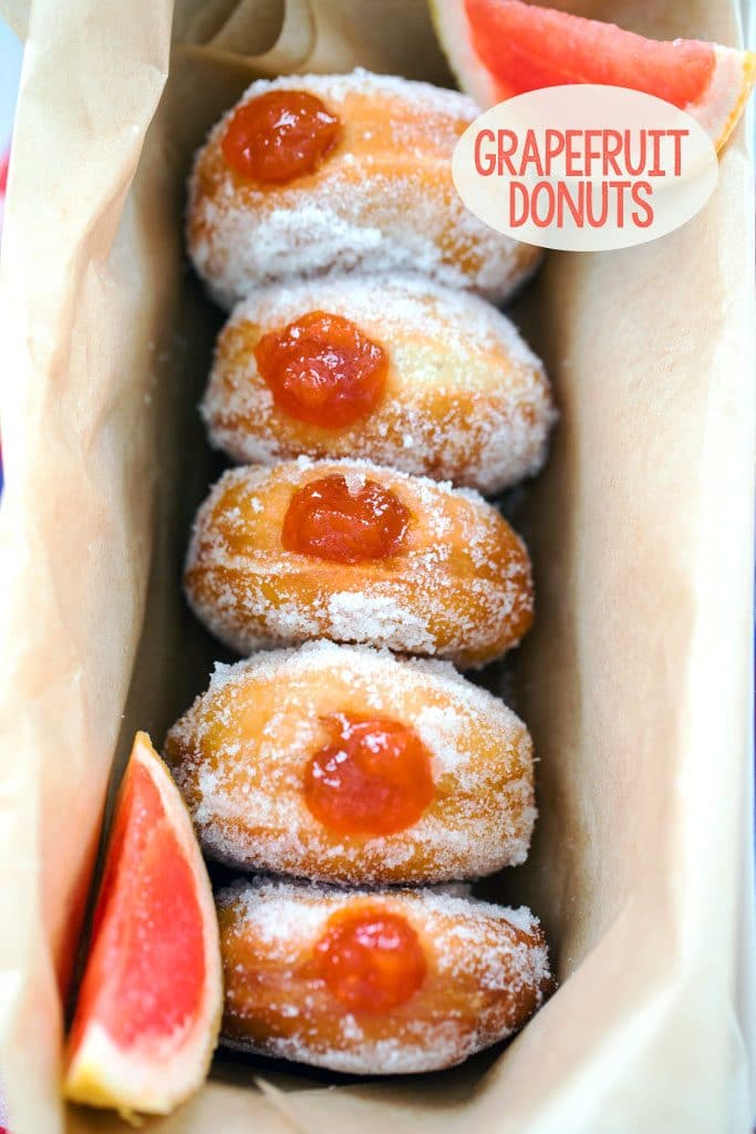 Bird's-eye view of five sugared donuts filled with grapefruit jam in a row in a loaf pan with "Grapefruit Donuts" text at the top