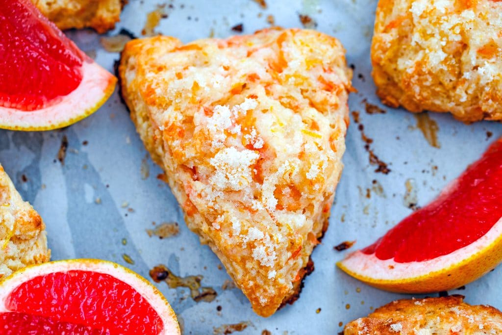 Landscape closeup view of grapefruit scone on a baking sheet with pink grapefruit segments and more scones around it