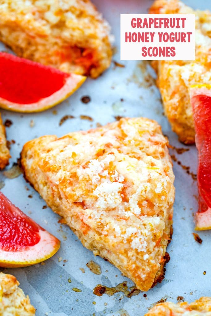 Overhead view of grapefruit scones on a baking sheet surrounded by pink grapefruit segments with the recipe title at top