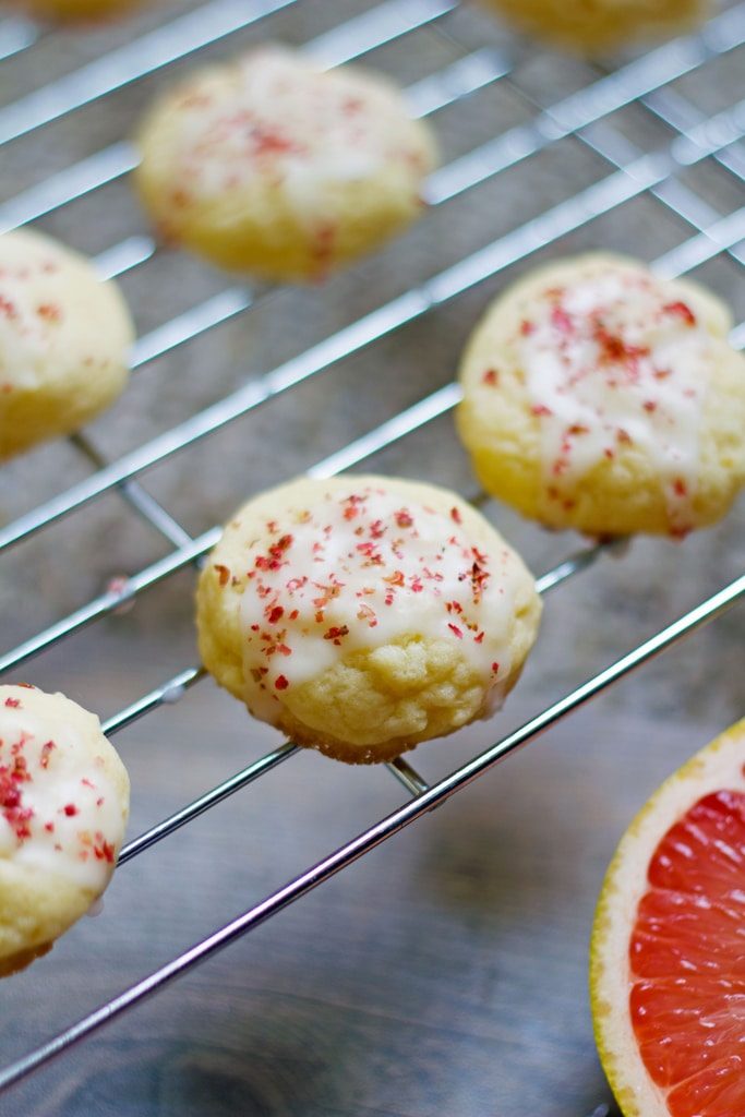 Several grapefruit pink peppercorn cookies on a cooling rack with a half a grapefruit