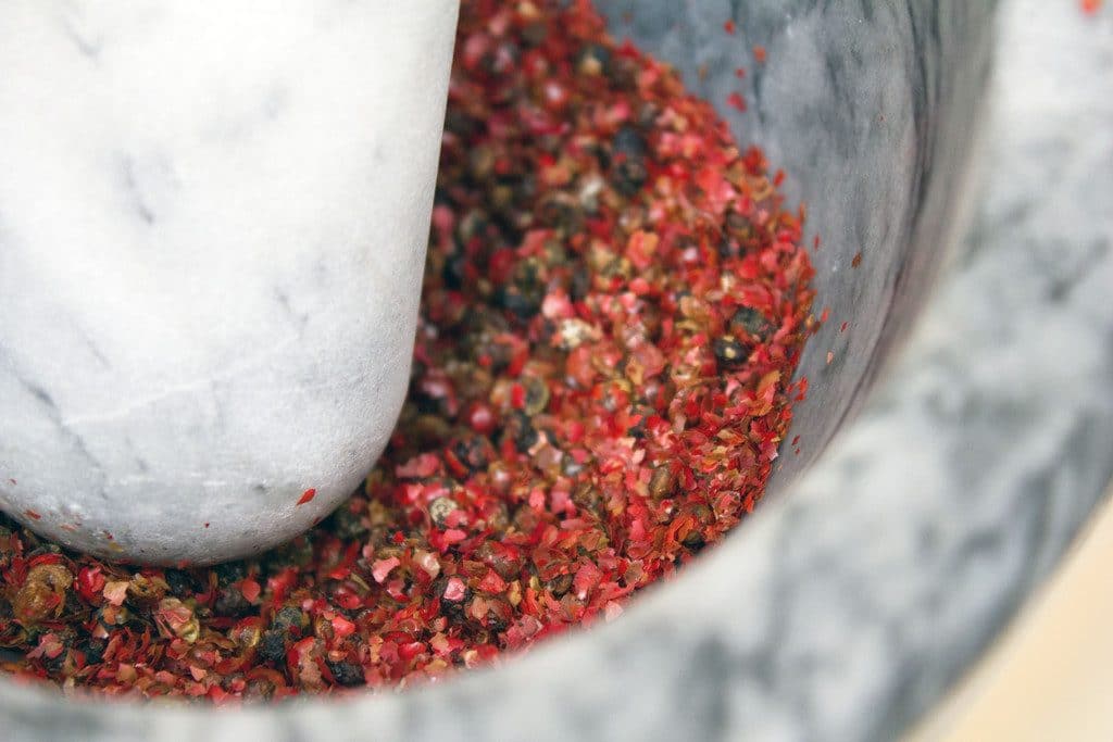 Pink peppercorns being crushed with a mortar and pestle