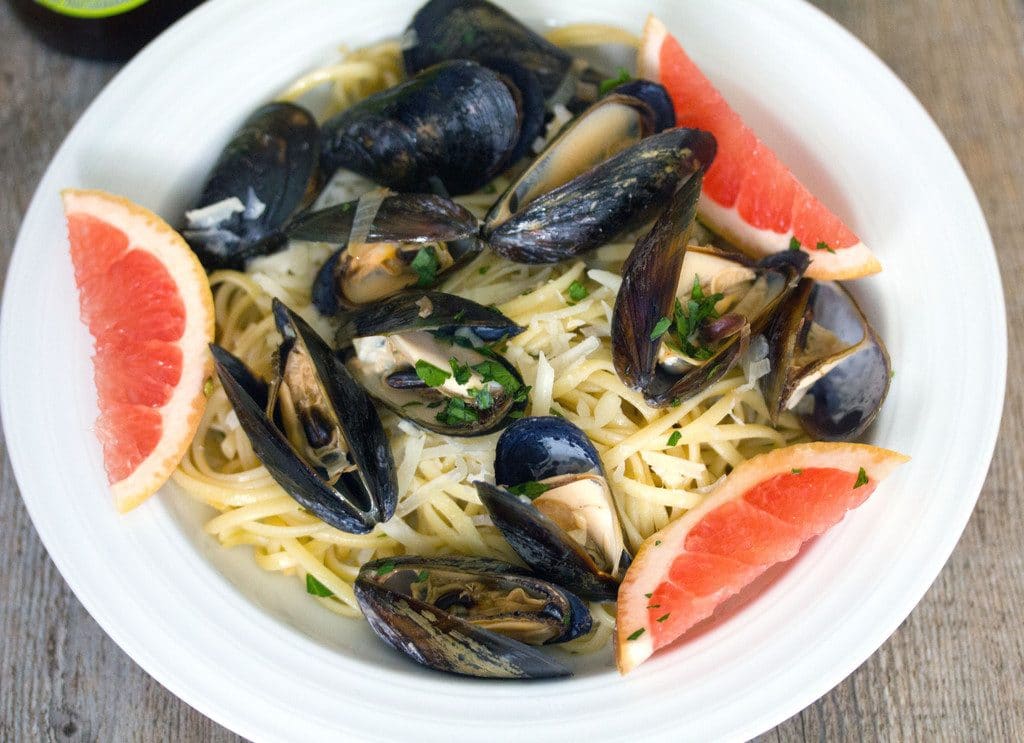 Landscape overhead view of grapefruit shandy mussels over linguine with grapefruit wedges in a white bowl