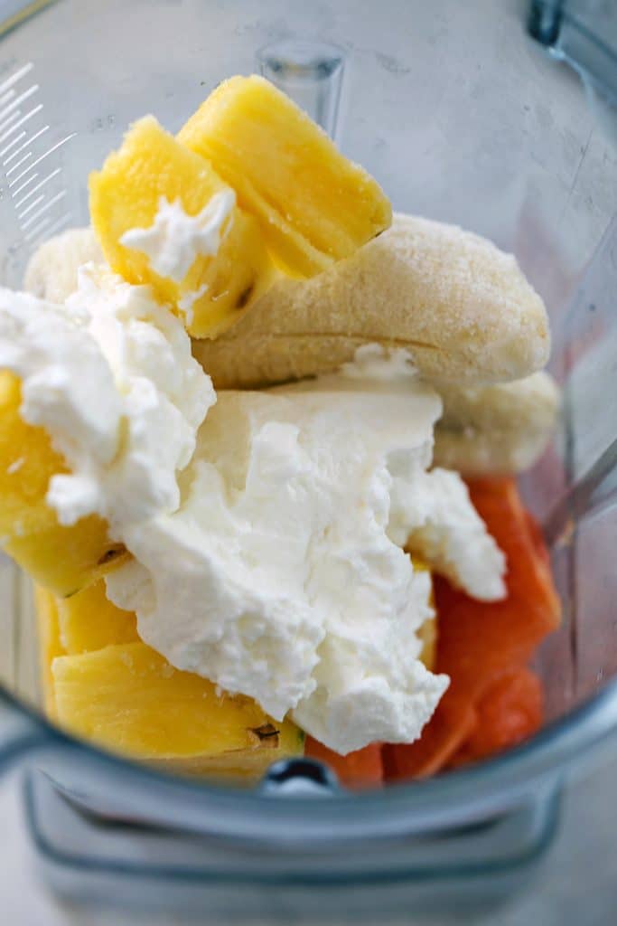 Blender with grapefruit sections, pineapple cubes, frozen banana, and Greek yogurt in it