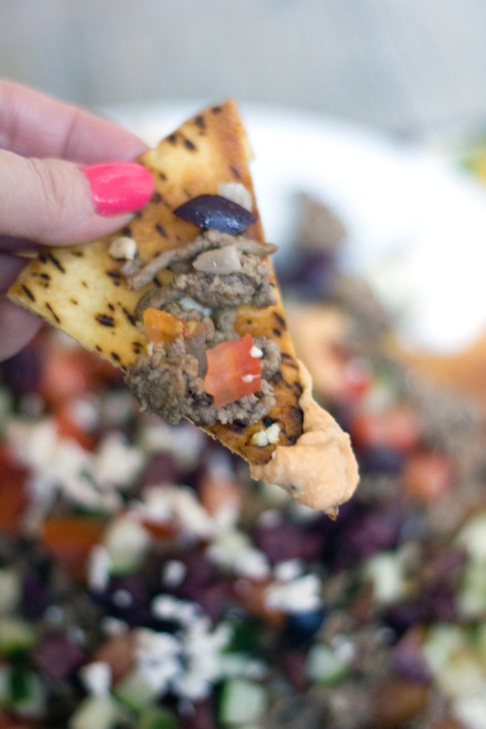 Image of hand holding pia chip with ground lamb, tomatoes, feta, and olives