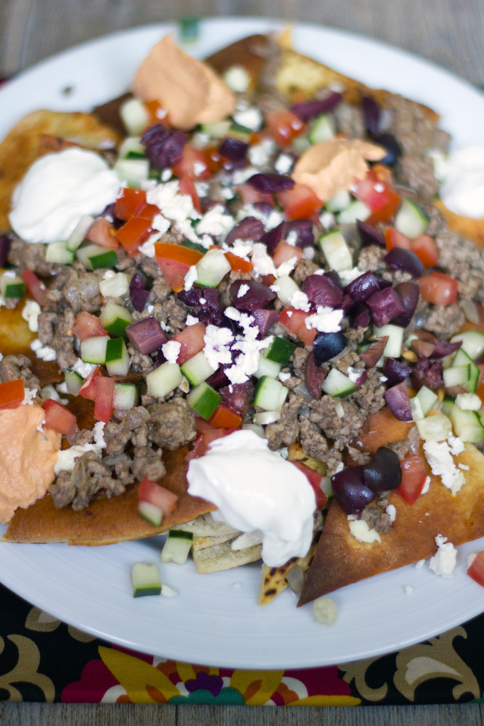 Overhead view of a plate of Greek nachos with ground lamb, feta cheese, cucumbers, tomatoes, olives, hummus, and yogurt